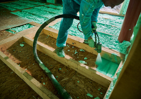 Male builder insulating wooden frame house. Cropped view of man worker spraying polyurethane foam on floor inside of future cottage, using plural component gun. Construction and insulation concept.の写真素材