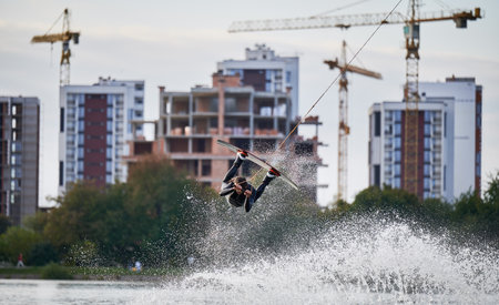 Wakeboarder making tricks while wakeboarding on lake. Young man surfer having fun wakesurfing in the cable park. Water sport, outdoor activity concept.の写真素材