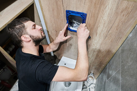 Bearded man holding screwdriver tool while installing toilet flush panel in apartment under...