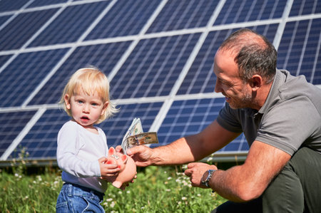 Father and his little son putting cash into piggy bank to save money on background of solar panels....