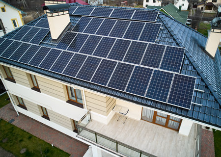 Aerial view of residential house with photovoltaic solar panel modules on rooftop. Home with solar electric system, lawn and pavement outside. Renewable energy and housing concept.の写真素材