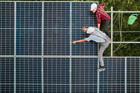 Aerial view of men technicians installing solar panels to high steel platform. Engineers wearing uniform and helmet. Concept of alternative energy.の写真素材
