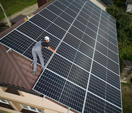 Man technician installing photovoltaic solar moduls on roof of house. Electrician in helmet building solar panel system outdoors. Concept of alternative and renewable energy. Aerial view.の写真素材