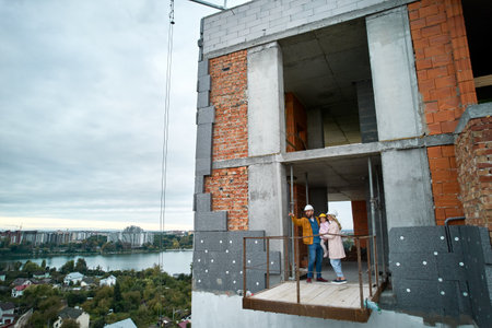 Man with wife and child standing inside residential building under construction. Urban district with newly constructed apartment building and family new residents real estate buyers. Drone viewの写真素材