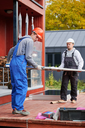 Installers building solar panel system. Men workers in helmets carrying photovoltaic solar module...
