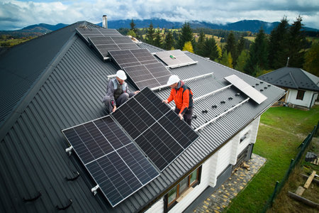 Engineers building photovoltaic solar module station on roof of house. Men electricians in helmets installing solar panel system outdoors. Concept of alternative and renewable energy. Aerial view.の写真素材