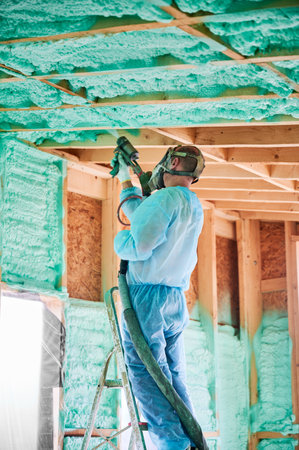 Male builder insulating wooden frame house. Man worker spraying polyurethane foam inside of future cottage, using plural component gun. Construction and insulation concept.の写真素材