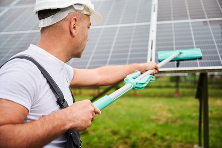 Close up view of adult worker cleaning PV battery by mop. Knowledgeable man taking care about green...