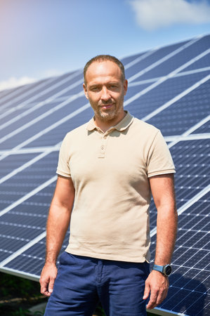 Portrait of man in casual clothes smiling to camera on background of solar panels. Innovations in green energy sources. Man showing his investment.の写真素材