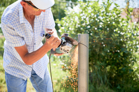 Male worker cutting metal pole with grinder. Man in protective glasses using hand-held grinder while preparing aluminum pole for solar panel installation.の写真素材