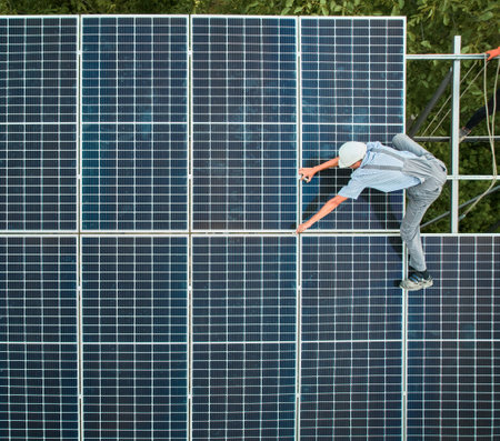 Aerial view of man technician installing solar panels to high steel platform. Engineer wearing uniform and helmet. Concept of alternative energy.の写真素材