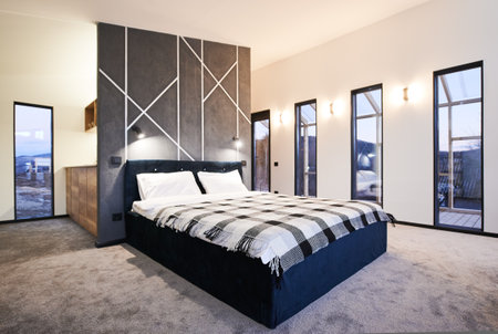 Minimalist interior of bedroom with big bed indoor. Front view of wide bed, with plaid blanket against gray wall with geometric ornament in sleeping area. Concept of interior.の写真素材