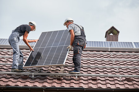 Men technicians lifting photovoltaic solar modul on roof of house. Electricians in helmets mounting solar panel system outdoors. Concept of alternative and renewable energy.の写真素材