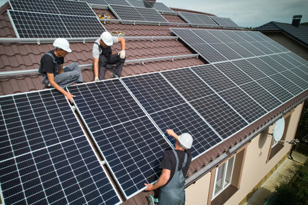 Men technicians mounting photovoltaic solar moduls on roof of house. Workers in helmets installing solar panel system outdoors. Concept of alternative and renewable energy. Aerial view.の写真素材