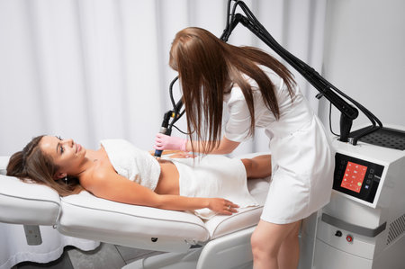 Beautician performing laser resurfacing of abdomen, ridding patient of stretched skin. Fractional CO2 laser is modern device for treatment of skin defects, scars and stretch marks after childbirth.の写真素材