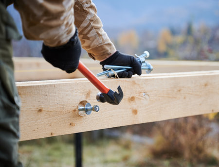 Man worker building wooden frame house on pile foundation. Carpenter hammering bolt into wooden truss, using hammer. Carpentry concept.の写真素材