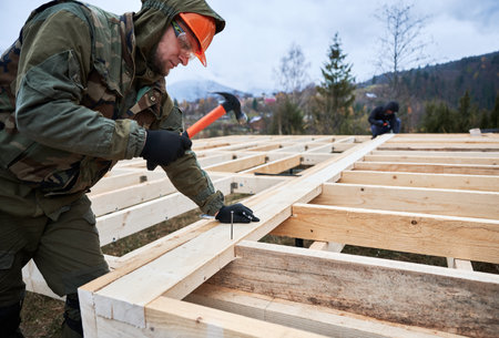 Man worker building wooden frame house on pile foundation. Carpenter hammering nail into wooden joist, using hammer. Carpentry concept.の写真素材