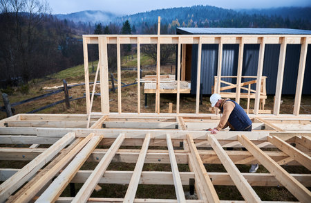 Man worker building wooden frame house on pile foundation. Carpenter hammering nail into wooden joist, using hammer. Carpentry concept.の写真素材
