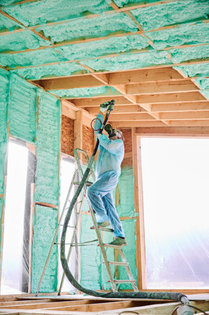 Male builder insulating wooden frame house. Man worker spraying polyurethane foam inside of future cottage, using plural component gun. Construction and insulation concept.の写真素材