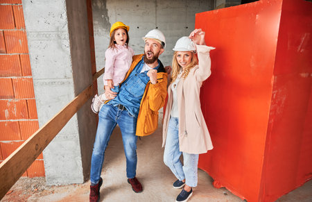 Man holding daughter and smiling. Happy couple real estate house buyers demonstrating keys from new home under construction. Family life and new home purchase concept.の写真素材