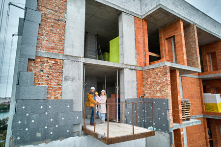 Man with wife and child standing inside residential building under construction. Urban district with newly constructed apartment building and family new residents real estate buyers. Drone viewの写真素材