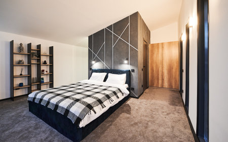 Minimalist interior of bedroom with big bed indoor. Front view of wide bed, with plaid blanket against gray wall with geometric ornament in sleeping area. Concept of interior.の写真素材