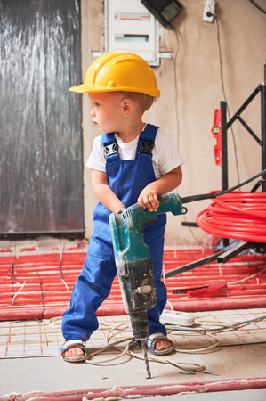 Child drilling floor with electric hammer drill at home during renovation. Kid construction worker using drilling machine while installing underfloor heating system in apartment.の写真素材
