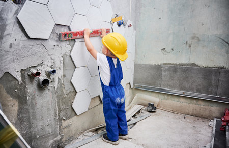 Little boy checking wall surface with spirit level in apartment. Kid in work overalls using level instrument while working on home renovation.の写真素材