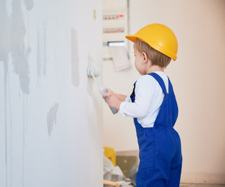 Child construction worker painting wall in apartment under renovation. Kid in safety helmet and work overalls using paint roller while working on home renovation.の写真素材
