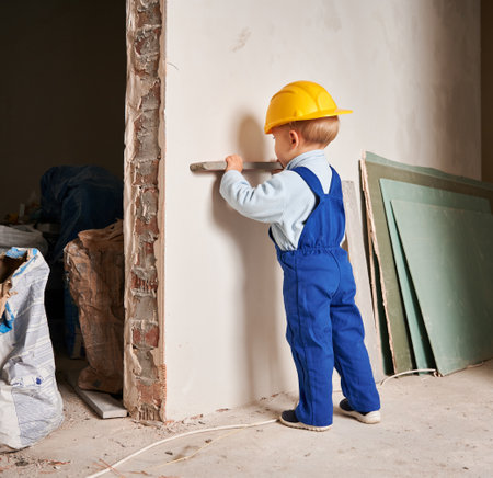Child construction worker holding spirit level instrument. Kid in safety helmet and work overalls playing in apartment under renovation.の写真素材