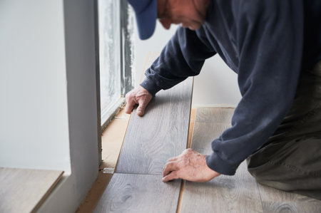 Close up of male builder laying laminate planks on the floor in flat under renovation. Male construction worker installing timber laminate flooring at home. Hardwood floor renovation concept.の写真素材