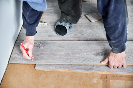 Close up of male construction worker with pencil in hand drawing line on laminate wooden panel. Man preparing laminate boards for floor installation in apartment under renovation.の写真素材