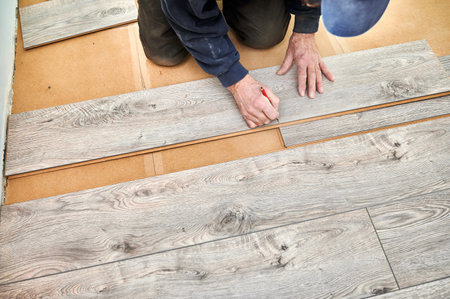 Close up of male construction worker with pencil in hand drawing mark on laminate wooden plank. Man preparing laminate boards for floor installation in apartment under renovation.の写真素材