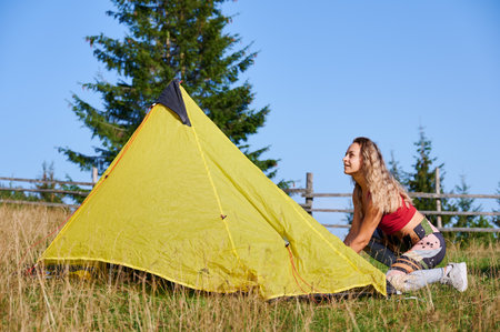 Woman hiker camping in mountains. Young female tourist putting tent, wearing sportswear, traveling. Concept of tourism and adventure.の写真素材