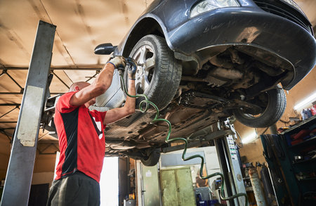 Mechanic, worker, repairman changing wheels of car in garage. Man wearing dirty gloves, working in servicing center, repairing cars. Concept of manual labor.の写真素材