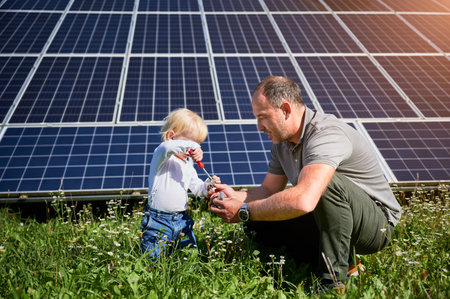 Dad showing to his little son how to use screwdriver in background of solar panels. Father teaching his child how to use tools. Son and his young dad learning tools.の写真素材