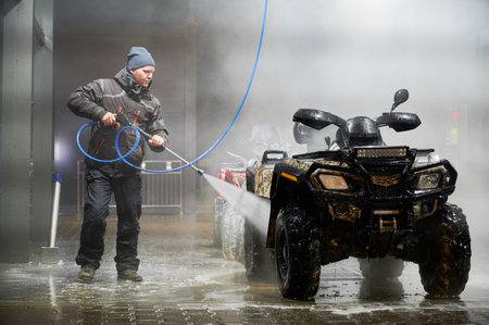 Full length of man cleaning quad bike with high pressure water sprayer at self-service car washing stationの写真素材