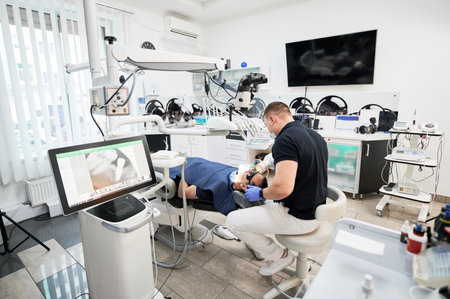 Dentist making X-ray, examining, inspecting problem, disease, holding equipment. Male doctor sitting on chair, fixing teeth, looking at screen. Concept of stomatology.の写真素材