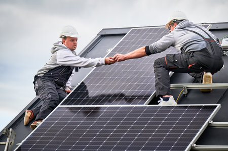 Workers building photovoltaic solar module station on roof of house. Men electricians in helmets installing solar panel system outdoors. Concept of alternative and renewable energy.の写真素材