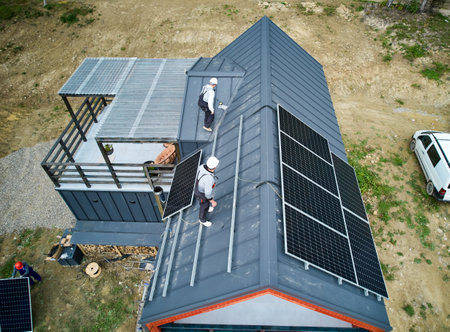 Men workers prepearing for mounting photovoltaic solar modules on roof of house. Electricians in helmets installing solar panel system outdoors. Concept of alternative and renewable energy.の写真素材