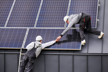 Installers building photovoltaic solar module station on roof of house. Men electricians in helmets installing solar panel system outdoors. Concept of alternative and renewable energy.の写真素材