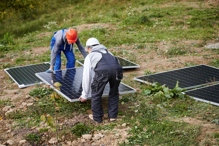 Workers building solar panel system. Men technicians in helmets carrying photovoltaic solar module outdoors. Concept of alternative and renewable energy.の写真素材