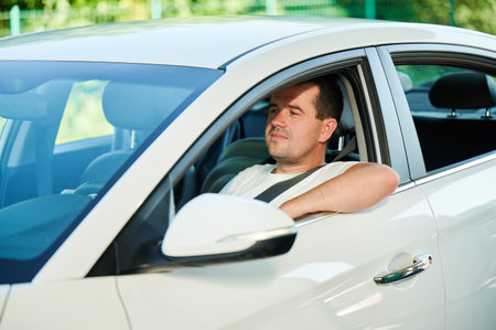 Confident man looking straight while sitting in white car. Adult man looking through window of his car.の写真素材