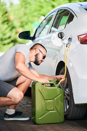 Suspicious man stealing gasoline from car tunk. Thief trying to pump fuel from someone elses automobile. Stealing fuel in broad daylight.の写真素材