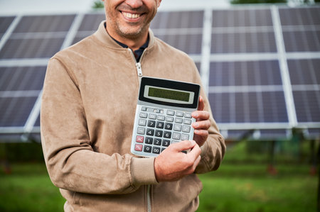 Smiling man showing future income from investing in alternative energy. Cropped picture of happy man demonstraiting big number on calculator. Man glad about huge sum profit.の写真素材