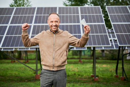 Man happy about money he earned by investing in alternative energy. Successful investment in green energy. Young male shouting cheers with money in hands.の写真素材