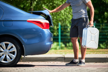 Man taking out canister with gasoline from car trunk. Cropped view of male adult taking out cistern with fuel to refuel his blue car.の写真素材