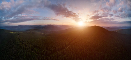 Beautiful landscape of hills with green coniferous trees, alpine path and mountain forest during sunset. Colorful dramatic evening sky with bright sun and clouds over mountain woods.の写真素材