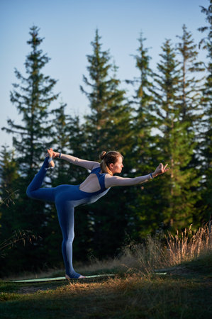 Young woman doing yoga asana Natarajasana. Sporty girl doing lord of the dance pose. Practicing gymtastic outdoor.の写真素材