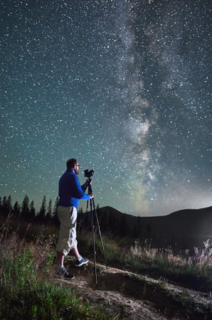 Professional photographer taking photos of Milky Way. Young male focusing his camera to take perfect picture of starry sky. Male taking pictures of night sky in mountains.の写真素材